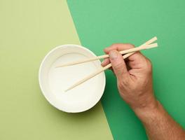 Pair of wooden chopsticks in a male hand and empty paper plate on a green background photo