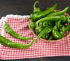 vainas de pimiento picante verde en una cesta de mimbre redonda sobre una mesa de madera marrón foto