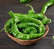 green hot pepper pods in a round wicker basket on a brown wooden table photo