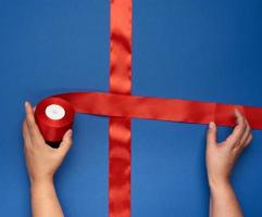 two female hands tie a red silk ribbon on a blue box, gift wrapping and decoration photo