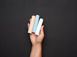 female hand holding three colored chalk on a background of an empty black chalk board photo