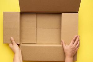 female hands are holding an empty open box of brown cardboard, top view photo