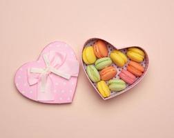 round baked multicolored macarons lie in a pink cardboard box in the shape of a heart photo