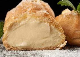 baked custard eclairs and sprinkled with powdered sugar and decorated with a mint leaf on a black board photo