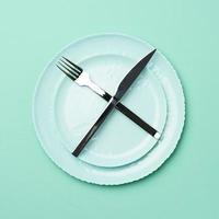 green round ceramic plate and crossed knife and fork on a green background, photo
