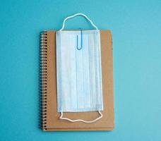disposable medical face mask and spiral paper notepad on blue background photo