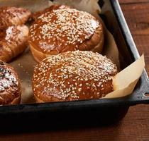 baked sesame buns on brown parchment paper, ingredient for a hamburger photo