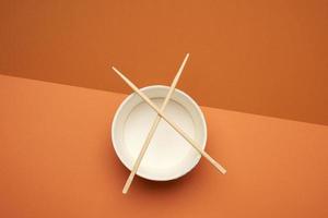 open empty noodle bowl and pair of wooden sticks on brown background photo
