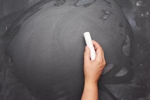 hand holds a piece of white chalk on the background of an empty black chalk board, presentation concept photo