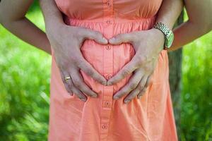 vientre embarazado con el símbolo del corazón de los dedos. foto