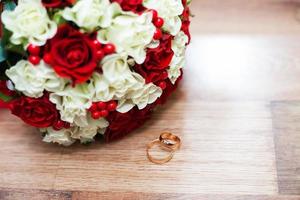 anillos y un ramo de novia de rosas rojas y blancas en la mesa
