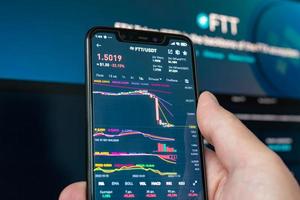 Man holding phone with FTX logo. Global fall of cryptocurrency graph - FTT token fell down on the chart crypto exchanges on app screen. FTX exchange bankruptcy and the collapse depreciation of token. photo