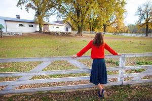 A beautiful girl in a red sweater stands with her back near a white wooden fence. Beautiful autumn. photo