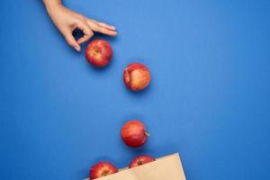 brown paper bag and ripe red apples, female hand pushing apples into packaging photo