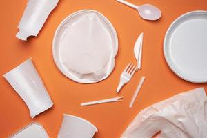 platos de plástico usados, piezas de plástico y una bolsa de plástico blanca sobre un fondo naranja foto