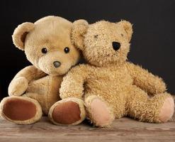 two brown teddy bears are sitting on a brown wooden table, black background photo