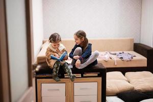 dos hermanas están sentadas en un sofá, mirando y leyendo un libro juntas. foto