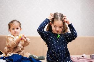 Two sisters are choosing clothes from the wardrobe at home on the sofa. Girl wears a starfish pendant around her neck. photo