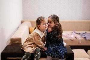 Two sisters sit on the sofa and tell and share girlish secrets with each other. photo