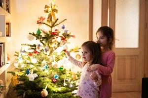 dos hermanas juntas cerca del árbol de navidad en casa por la noche. foto