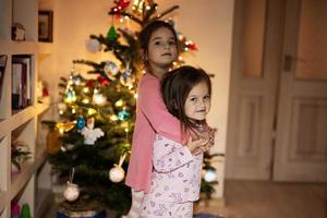 dos hermanas juntas cerca del árbol de navidad en casa por la noche. foto