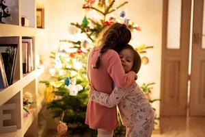 Two sisters together near Christmas tree at evening home. photo