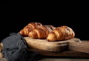 baked croissants on brown kitchen board, black background photo