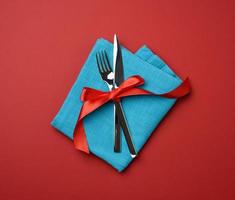 metal fork and knife tied with a red silk ribbon, red background photo