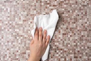 female hand wipes a brown table with a white rag photo