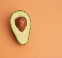 aguacate verde medio maduro con un hueso marrón sobre un fondo naranja abstracto foto