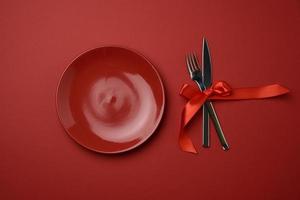 placa de cerámica vacía redonda roja y tenedor y cuchillo de metal atados con una cinta de seda roja foto