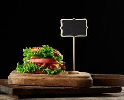 cheeseburger with minced meat, green lettuce and ketchup on a wooden brown kitchen board photo