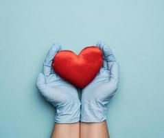 two hands in blue latex gloves holding a red textile heart, donation concept photo