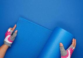 two female hands in sports gloves unfold a blue yoga mat photo