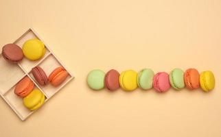 baked multi-colored macarons cookies lie in a row on a beige background, top view photo