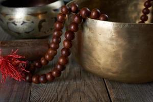 Cuenco tibetano de cobre cantando con un badajo de madera y un rosario de oración sobre una mesa de madera gris foto