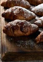 baked croissants sprinkled with powdered sugar lie on a brown wooden board photo
