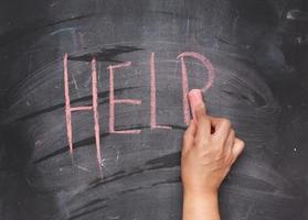 female hand with red chalk writes help on a black chalk board photo