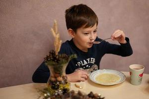 Boy has dinner in kitchen, eat bouillon. photo