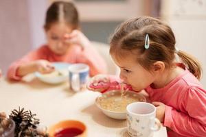 Two sisters have dinner together in the kitchen, baby girl eats bouillon. photo