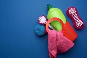 pink basket with washing sponges, brushes and cleaning agent in a green plastic bottle on a blue background photo