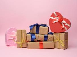 stack of gifts wrapped in brown kraft paper and tied with silk ribbon, boxes on a pink background photo