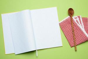 open notebook with blank white sheets and wooden spoon on green background photo