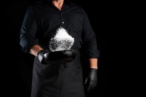 man in a black uniform holding a round cast iron pan with salt photo