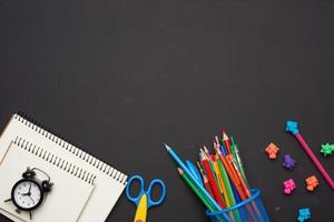 lápices de madera de colores, tijeras, blocs de notas en una pizarra negra en blanco foto