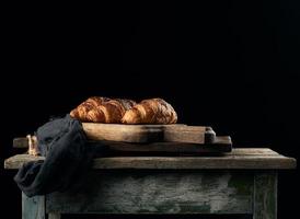 croissants horneados en tablero de cocina marrón, fondo negro foto