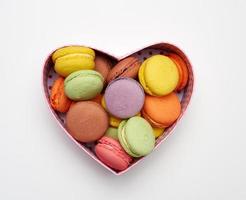 round baked multicolored macarons lie in a red cardboard box in the shape of a heart photo