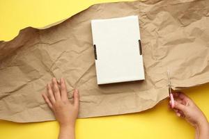 caja rectangular de cartón blanco y dos manos femeninas envueltas con papel marrón sobre un fondo amarillo foto