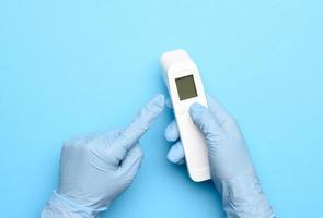 two hands in blue latex gloves hold an electronic thermometer to measure temperature photo