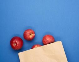 manzanas rojas maduras en una bolsa de papel marrón, fondo azul foto